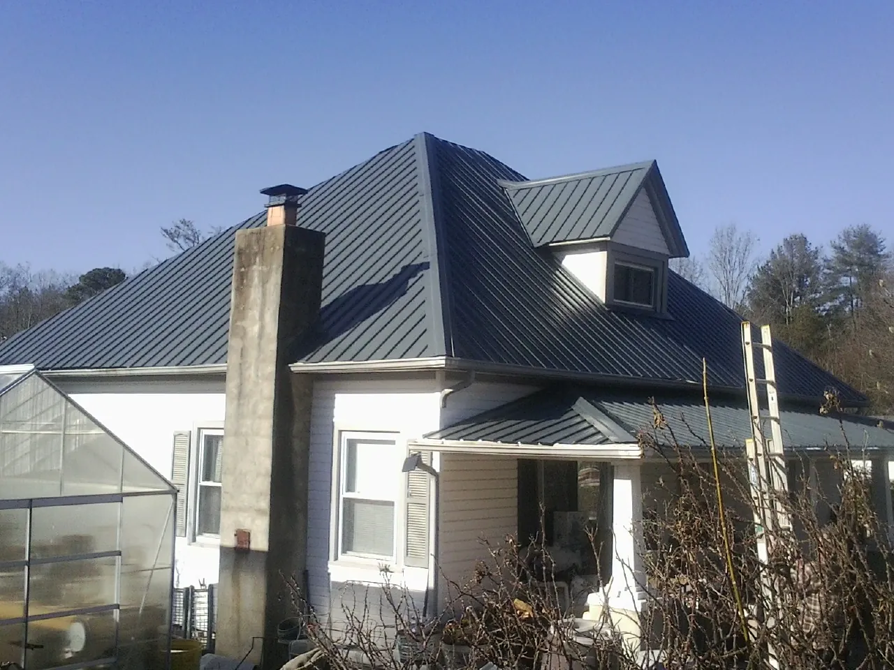 Dark blue standing seam metal roof on a white farmhouse with dormer — Slate & Tile Roof Repair by Roofing Brothers in Fulshear