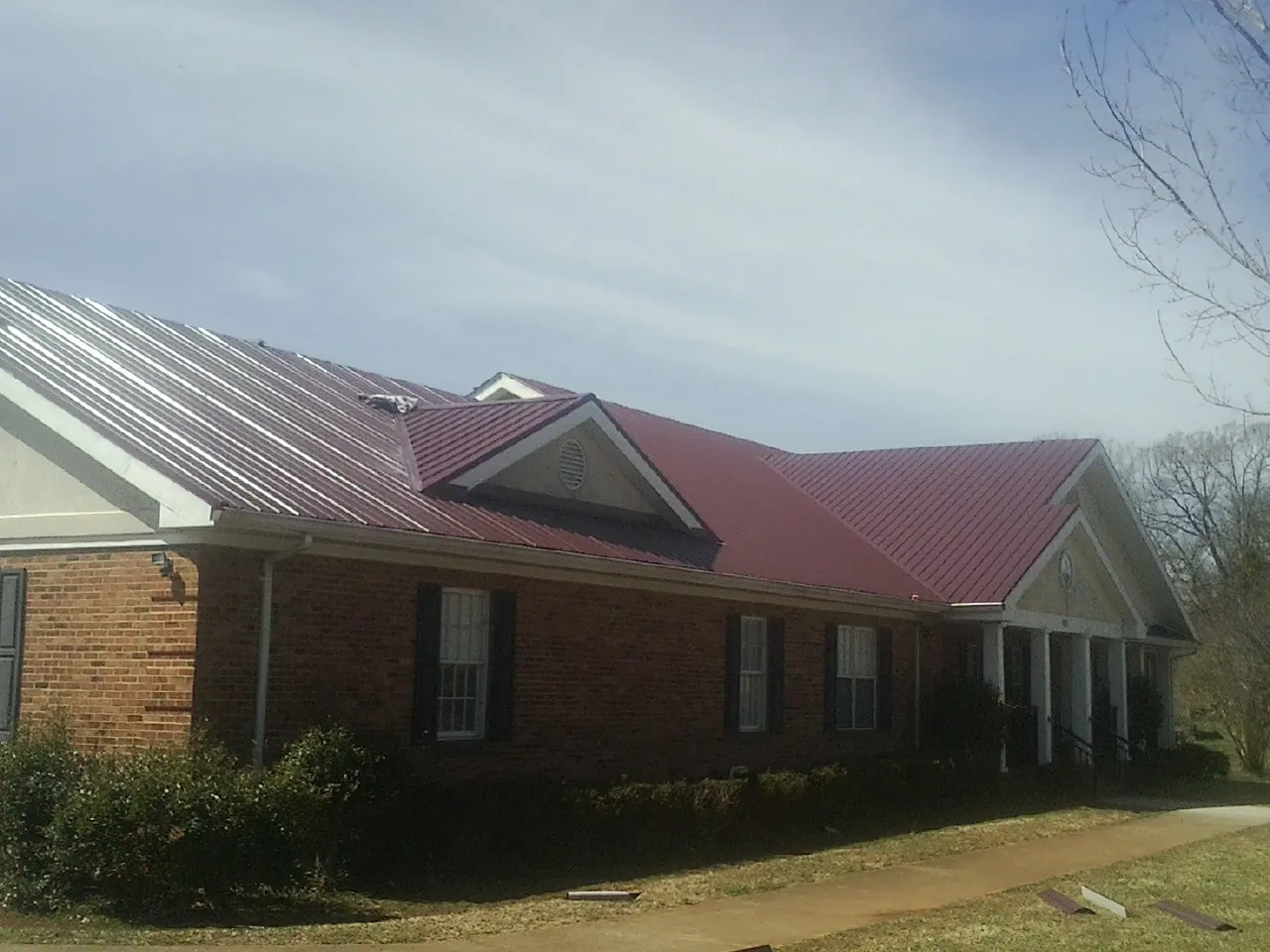 Red metal roof with gabled entries on a long brick building, from a Hail Damage Roof Repair job in Fulshear