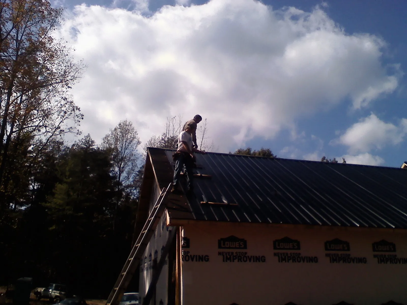 Roofer fastening dark metal panels high against a cloudy sky, from a Roof Inspection job in Fulshear