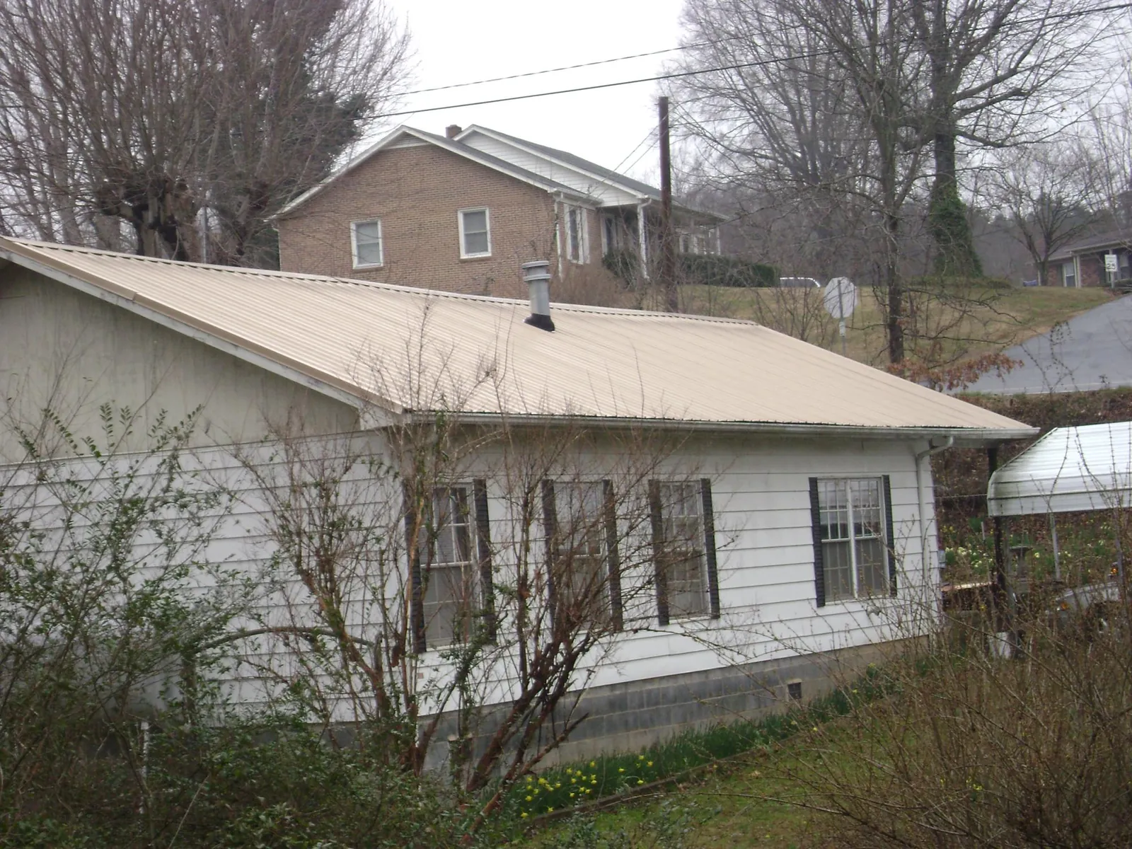 Tan metal roof on a white sided house set into a hillside — Commercial Roofing by Roofing Brothers in Fulshear